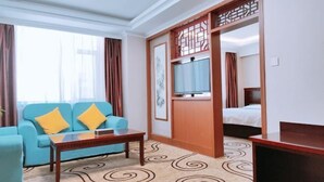 A hotel room with a blue sofa, a wooden coffee table, a bed with white bedding, and a television on a wooden stand. - Dongying Garden Hotel (Lanzhou University Railway Station) (Lanzhou)