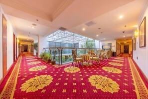A hotel corridor with a red carpet, a dining area with chairs and a table, and a large window.