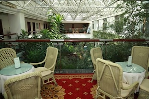 Un balcon agrémenté de fauteuils et d’une table en osier, donnant sur un jardin intérieur luxuriant et un coin repas.