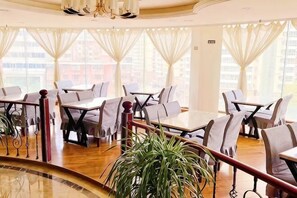 A restaurant with tables and chairs, large windows, and a plant.