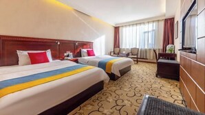 Habitación de hotel con dos camas, un escritorio, una silla, un televisor y una ventana con cortinas.
