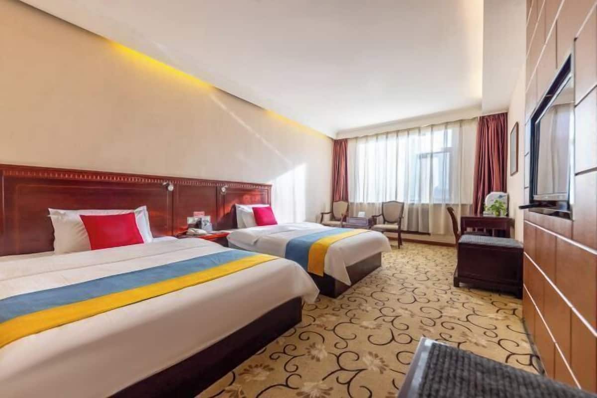 Habitación de hotel con dos camas, un escritorio, una silla, un televisor y un amplio ventanal con cortinas.
