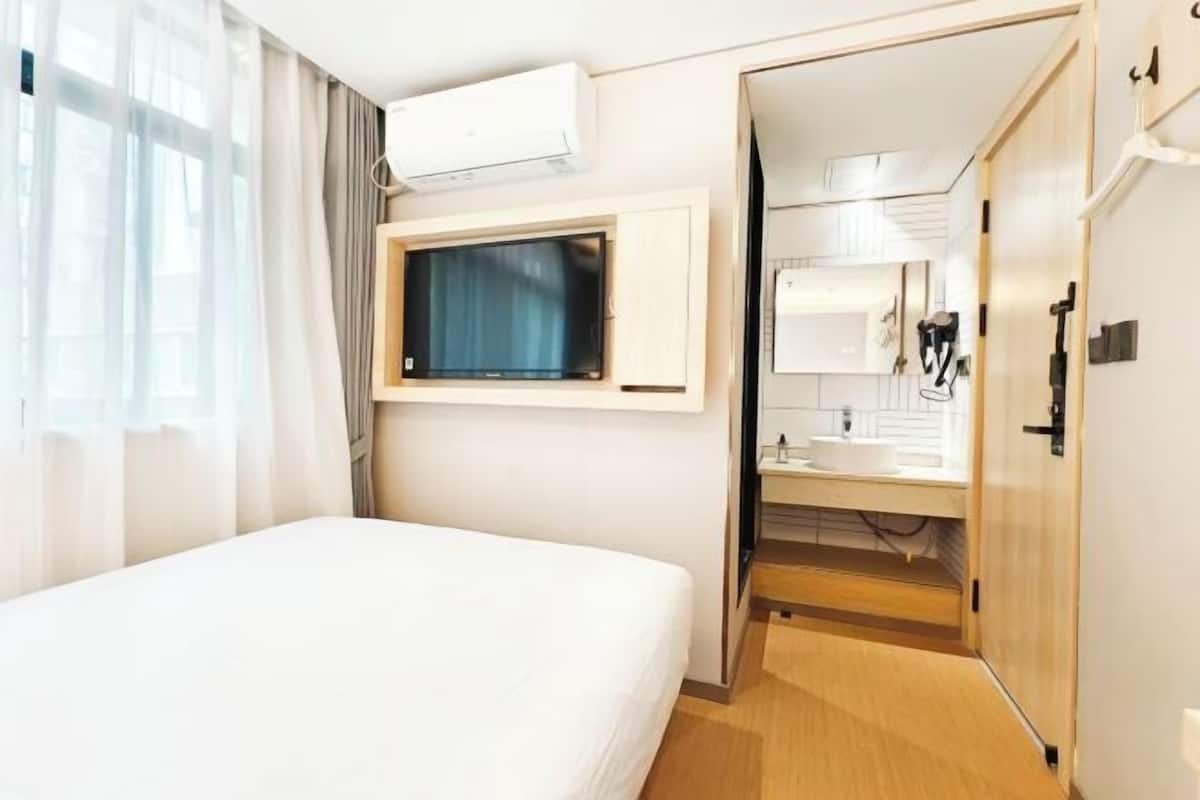 Een hotelkamer met een bed, een wandtelevisie, een badkamer met een wastafel en spiegel, en een airconditioning.