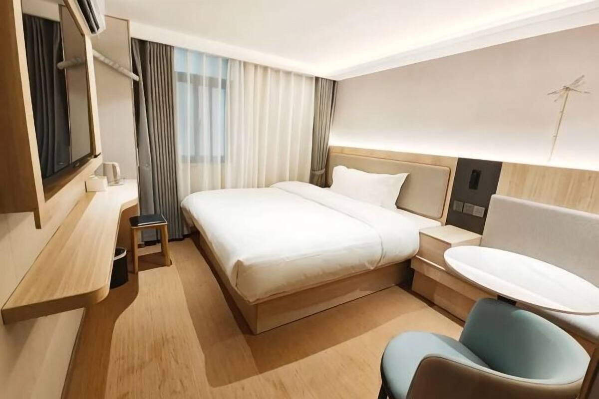 Een hotelkamer met een bed, nachtkastje, stoel, bureau en een klein tafeltje.