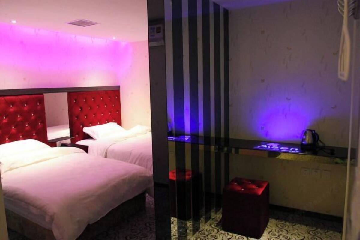 Een hotelkamer met een rode, gestuufde hoofdeinde, twee bedden, een klein tafeltje met een waterkoker, en een kamer met een patroon vloer.