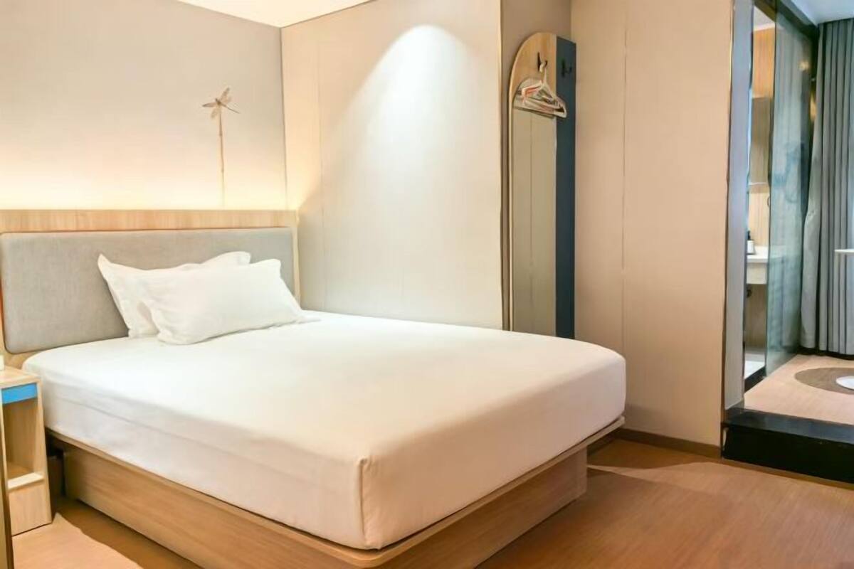Een moderne hotelkamer met een bed, nachtkastje en een spiegel.