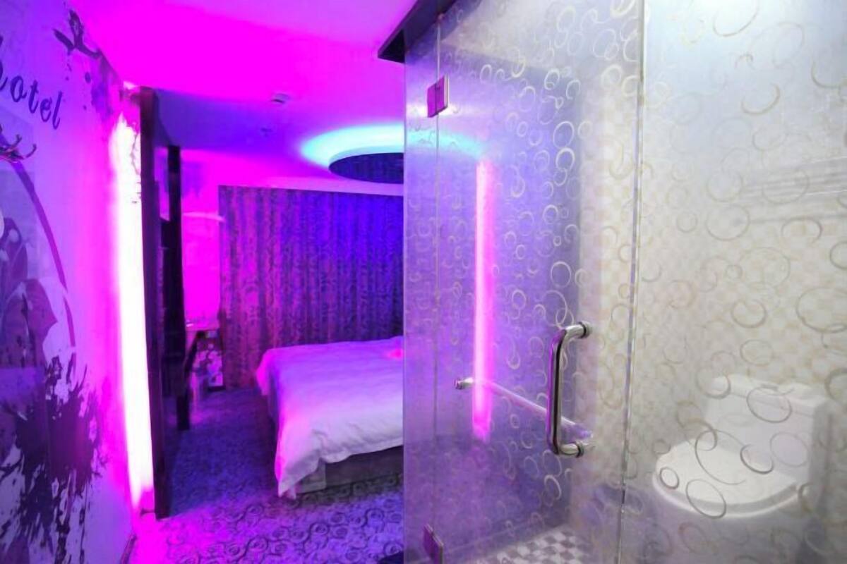 Een hotelkamer met een bed, een glazen douchecabine en een behang met patroon.