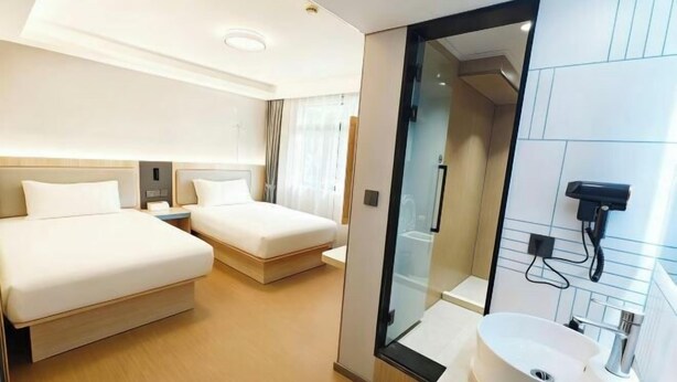 A hotel room with two beds, a glass-enclosed shower, and a sink. - fengyuhotel (Shanghai)