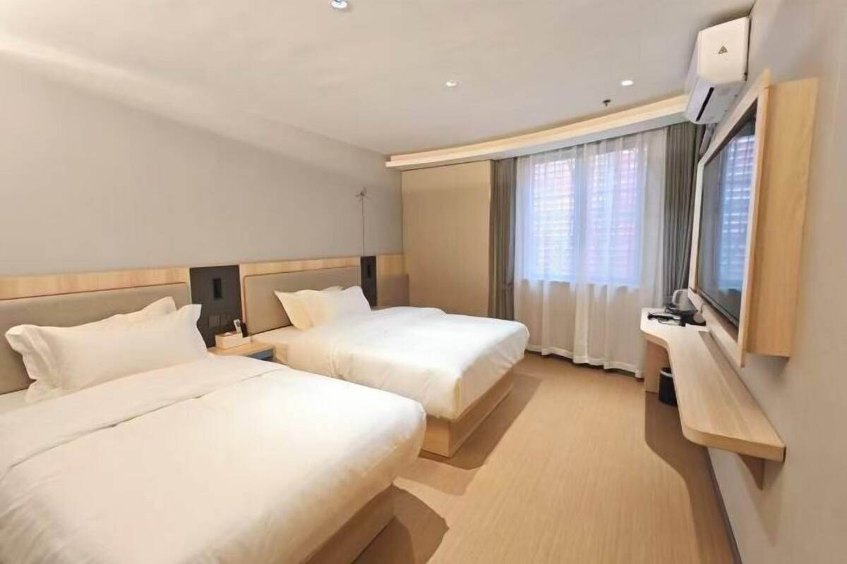 Een hotelkamer met twee bedden, een bureau, een televisie en een raam met gordijnen.