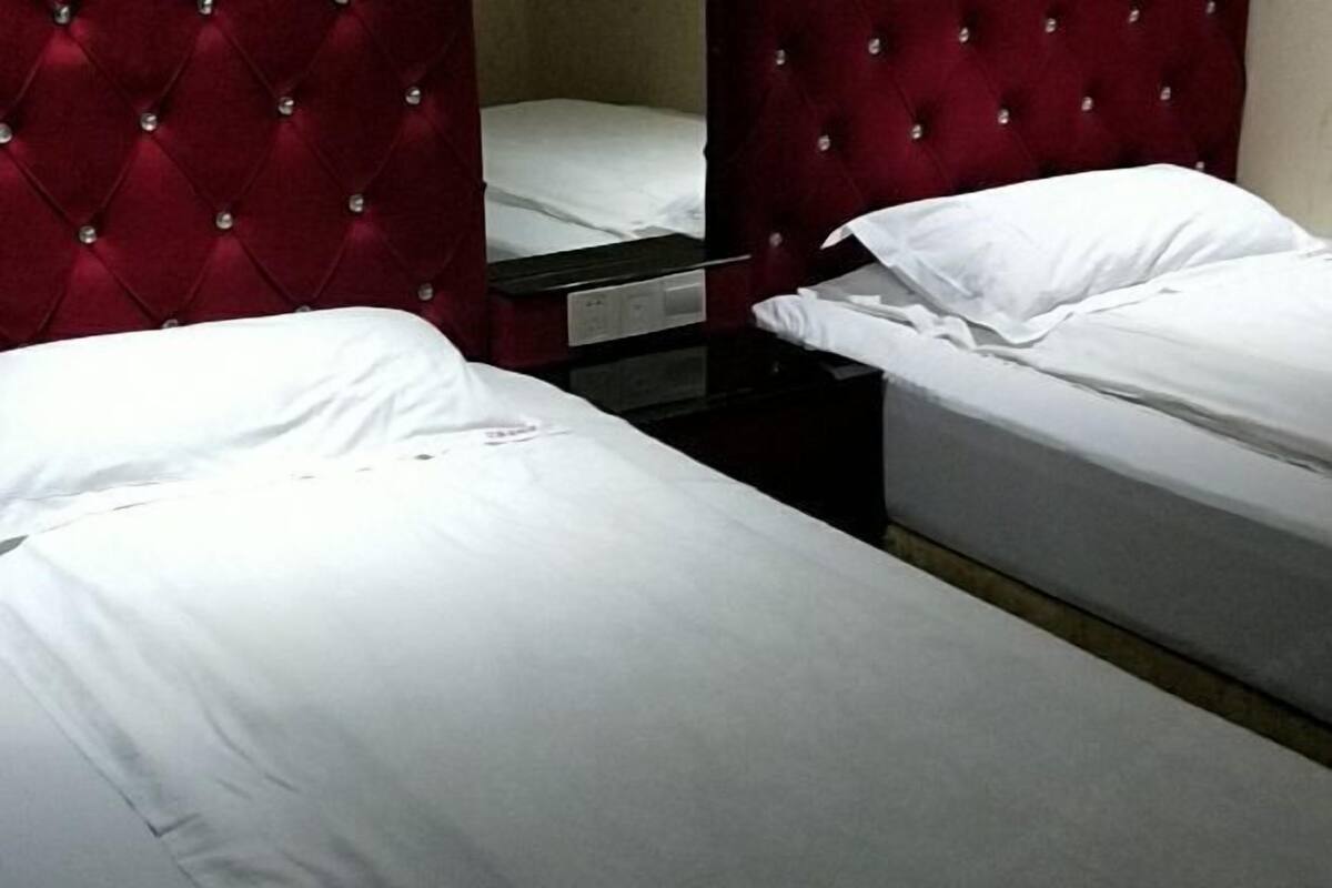 Een hotelkamer met twee enkele bedden, een rode, gestoffeerde hoofdbord en een klein nachtkastje.