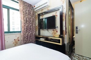 Una habitación de hotel con cama, televisión montada en la pared, aire acondicionado y una puerta.