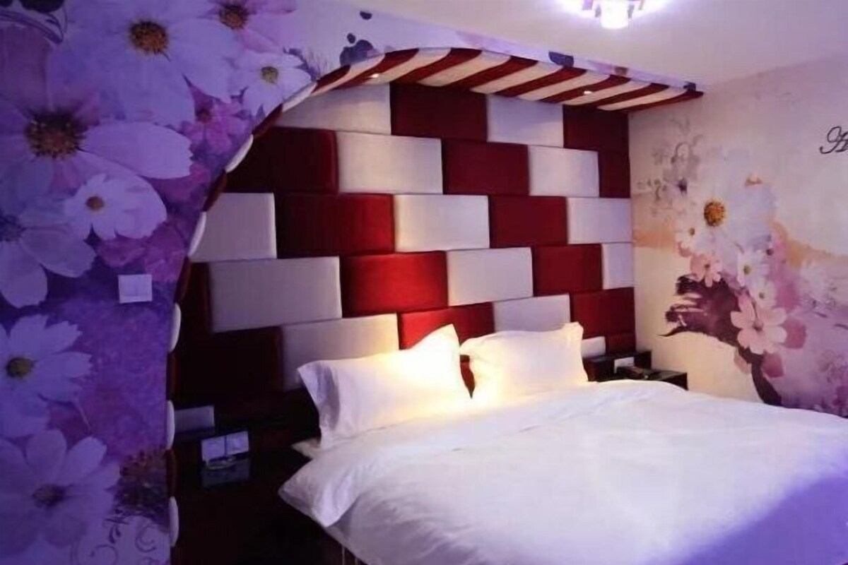 A bedroom with a modern headboard, a floral bedspread, and a nightstand with a lamp.