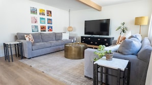 Un salon moderne avec un canapé gris, une table basse, un téléviseur et une bibliothèque.