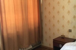 A hotel room with a bed, a nightstand, a wall clock, and a window with curtains. - Ali Pulan Town Hotel (Purang)