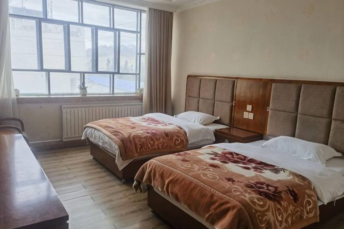 A hotel room with two beds, a wooden headboard, a window with a view, and a radiator.