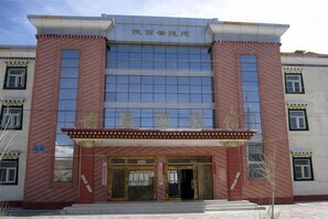 A building with a large glass facade, a red brick exterior, and a sign above the entrance. - Ali Pulan Town Hotel (Purang)