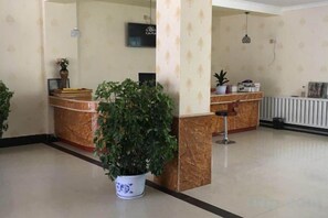 A reception area with a marble counter, a potted plant, and a television mounted on the wall. - Ali Pulan Town Hotel (Purang)