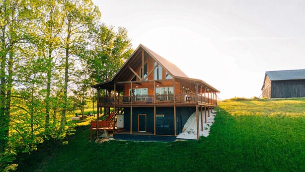 Une grande maison en bois dotée d’un balcon, entourée d’une pelouse et d’arbres.
