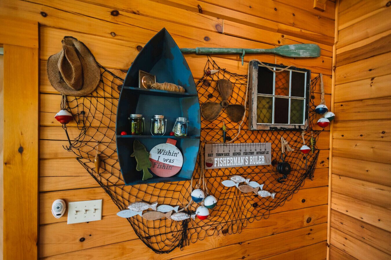 A fisherman's ruler, fishing hooks, a fishing net, and a hat on a wooden wall.