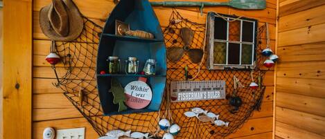 A fisherman's ruler, fishing hooks, a fishing net, and a hat on a wooden wall.