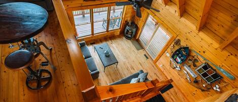 Interior de cabana com piso de madeira, mesa de jantar, sofá, bicicleta e vara de pesca.