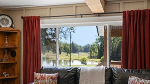 Un salon avec un canapé en cuir, des rideaux rouges et une vue sur un lac et des arbres.