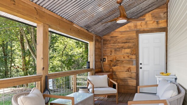 Une cabane en bois avec un porche, des meubles blancs et une porte.