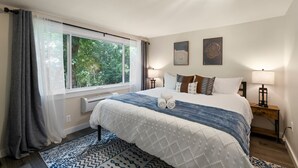 Une chambre à coucher avec un grand lit, deux lampes de chevet, une fenêtre avec des rideaux et un climatiseur fixé au mur.