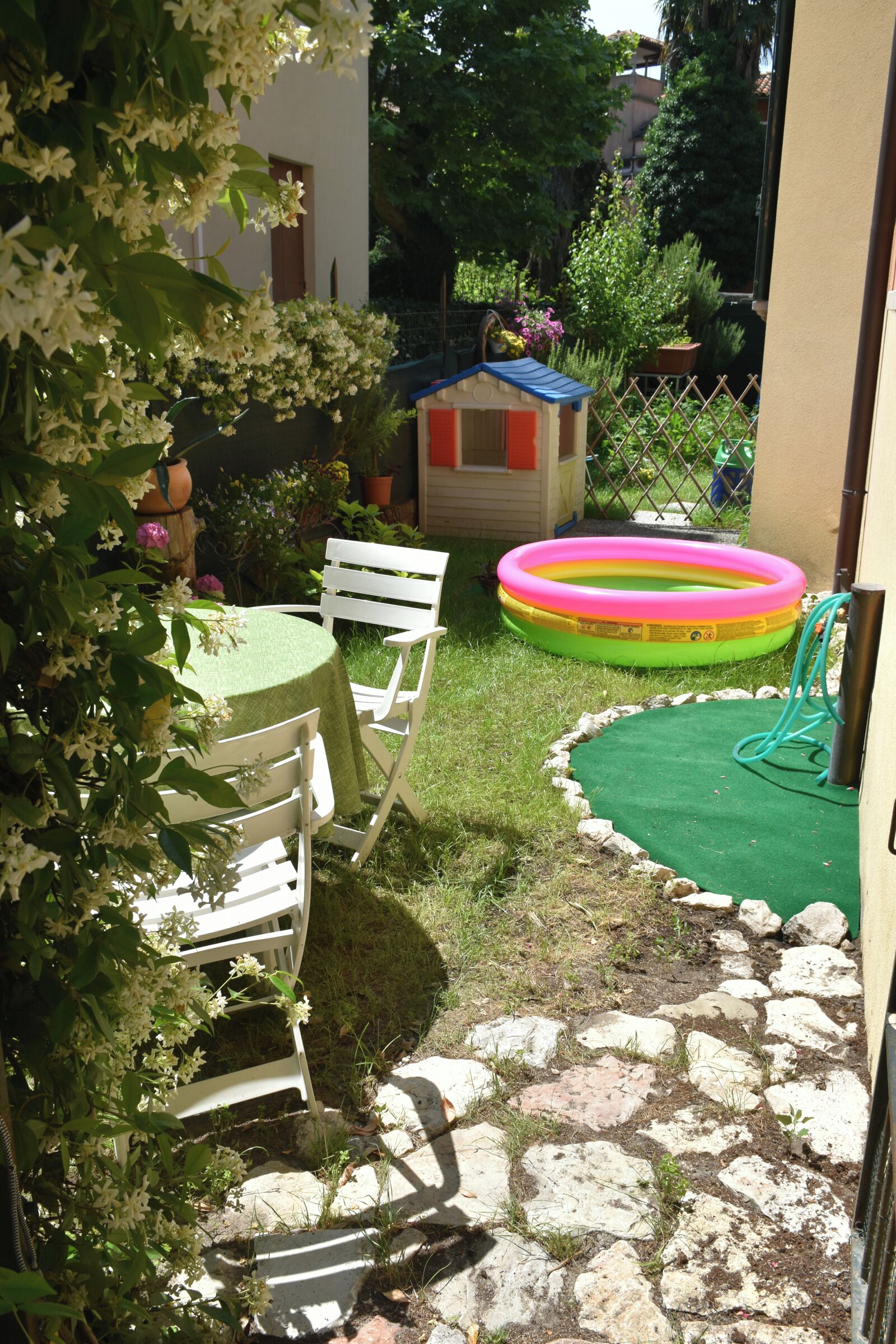 Une terrasse avec une table et des chaises, une petite maison de jeu et une piscine gonflable colorée.