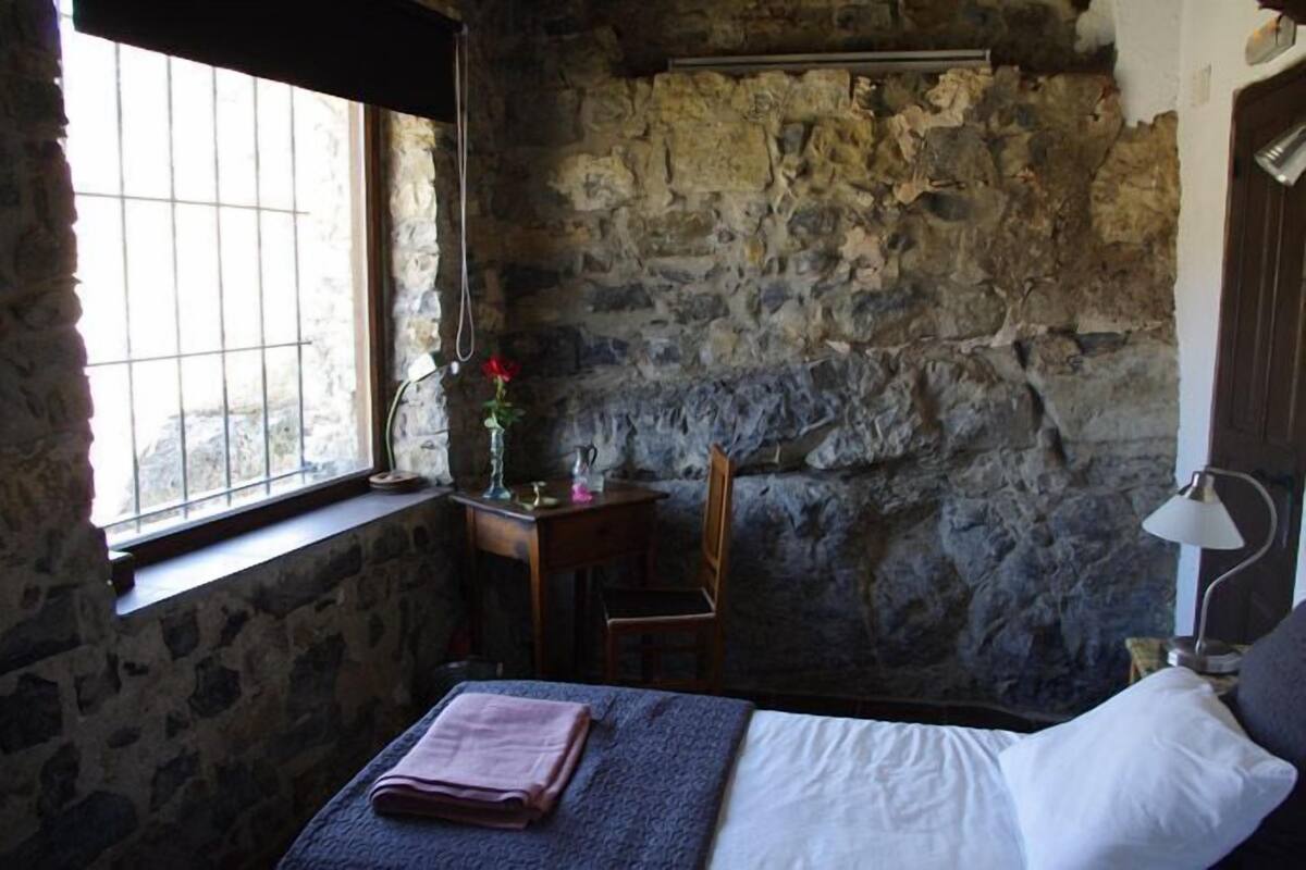 A stone-walled room with a bed, a desk, and a chair.