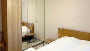 A bedroom with a bed, a wooden wardrobe, a small table, and a chair. - Cozy 2-bedroom Apartment Near Koksijde Beach (Koksijde)