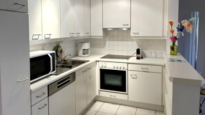 A compact kitchen with white cabinets, a microwave, a coffee maker, an oven, and a sink. - Cozy 2-bedroom Apartment Near Koksijde Beach (Koksijde)