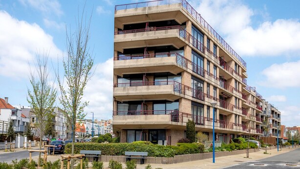 A multi-story building with balconies, a parking area, and a street view. - Cozy 2-bedroom Apartment Near Koksijde Beach (Koksijde)