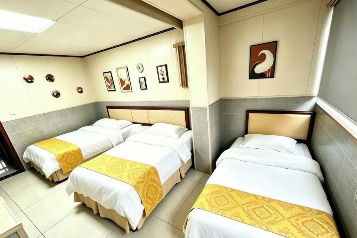 A hotel room with three single beds, a small table, and a wall with framed pictures.