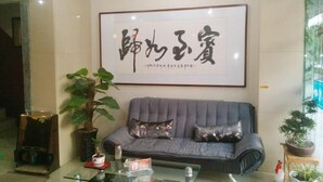 A room with a grey sofa, a framed calligraphy piece on the wall, and a potted plant beside the sofa.