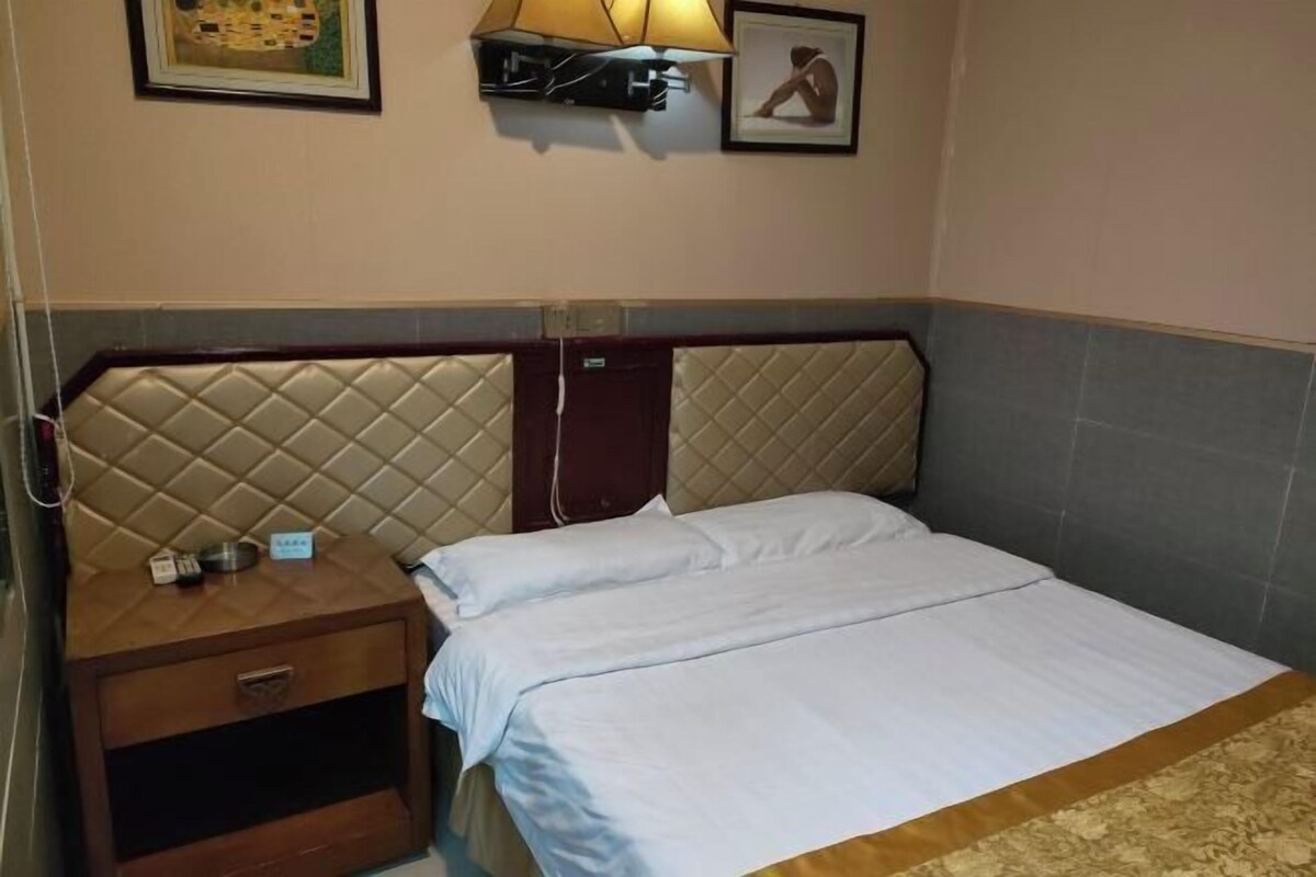A hotel room with a bed, a nightstand, a lamp, and a picture on the wall.