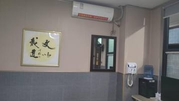A hotel room with a bed, a framed calligraphy piece, a mirror, a phone, and a water dispenser.