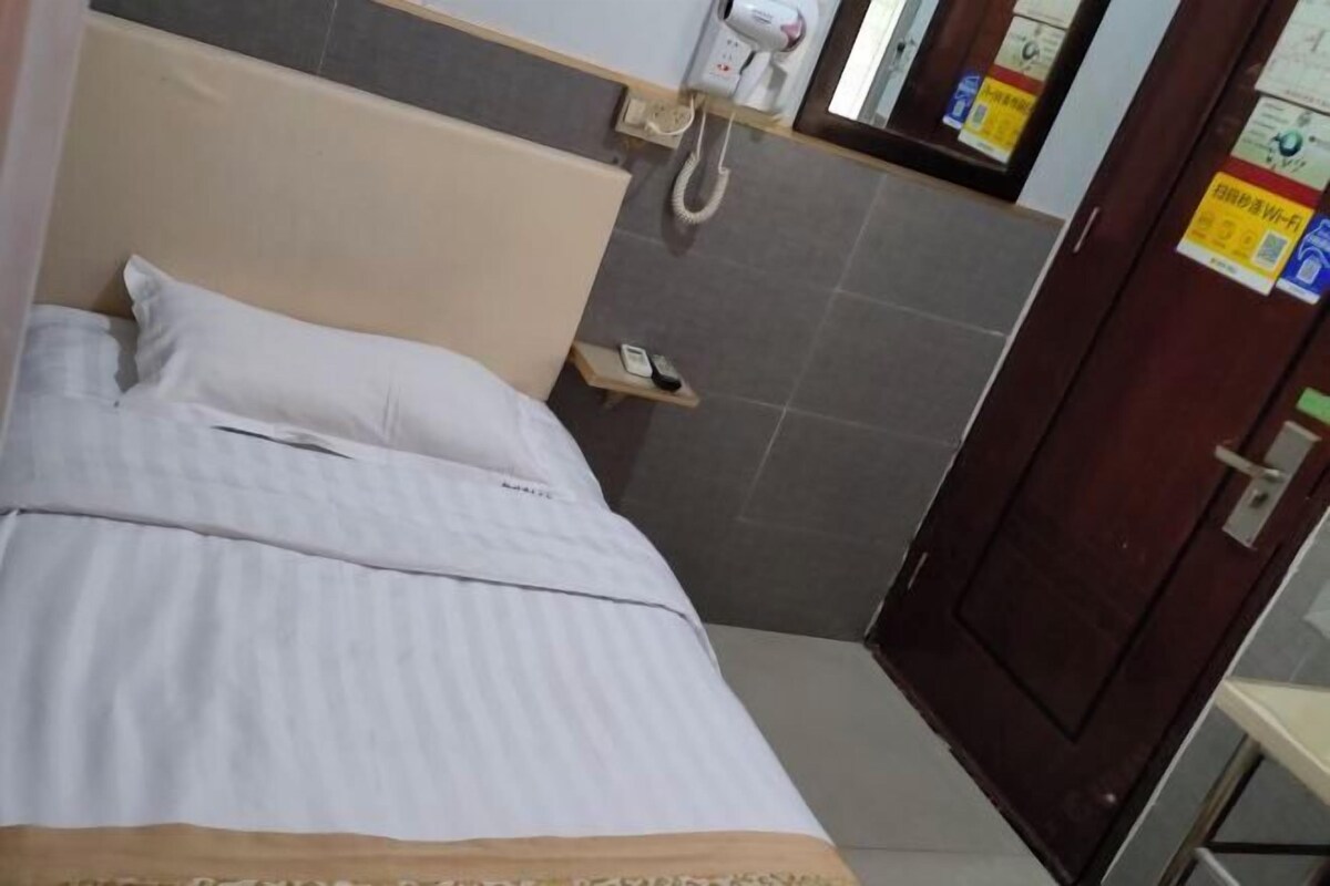 A hotel room with a bed, a bedside telephone, a small table with a phone, and a door with a sign.