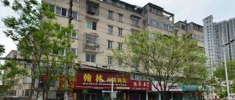 A multi-story building with commercial establishments on the ground floor, surrounded by trees and a sidewalk.
