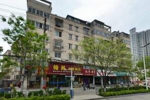 A multi-story building with commercial establishments on the ground floor, surrounded by trees and a sidewalk. - Hanlin Business Hotel (Huaibei)