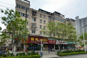 Un edificio de varios pisos con locales comerciales en la planta baja, rodeado de árboles y una acera.