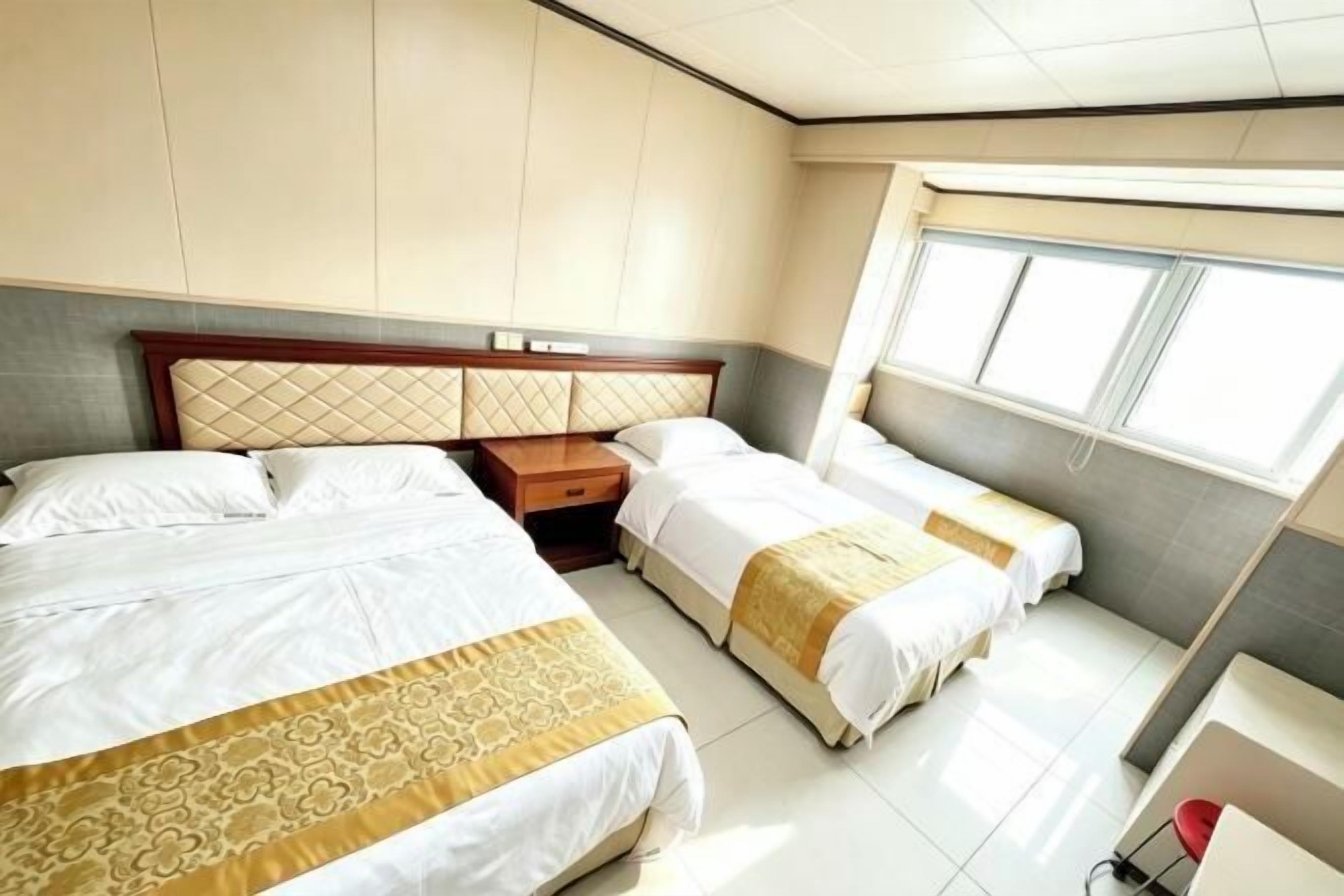 A hotel room with two beds, a nightstand, a window, and a small desk.