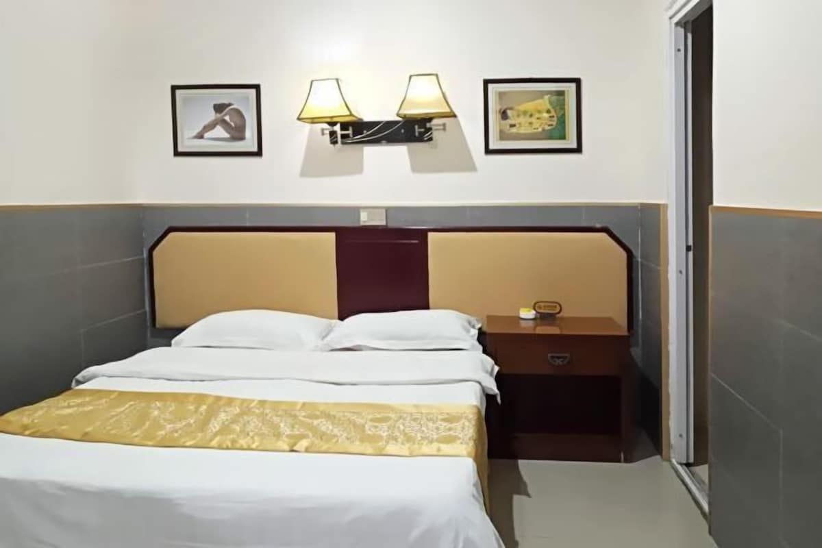 A hotel room with a bed, bedside table, lamp, and two framed pictures on the wall.