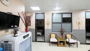 A hotel room with a bed, a TV, a heater, two chairs, a small table, and a window.