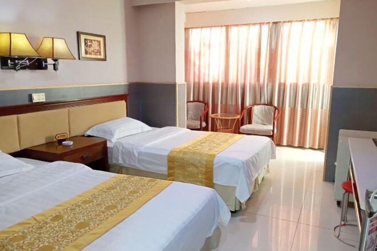A hotel room with two beds, a desk, a chair, a lamp, and a window with curtains.