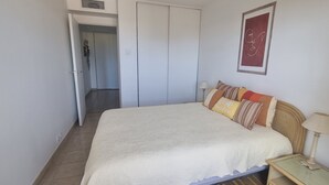 A bedroom with a bed, pillows, a nightstand, a lamp, and a door leading to another room.