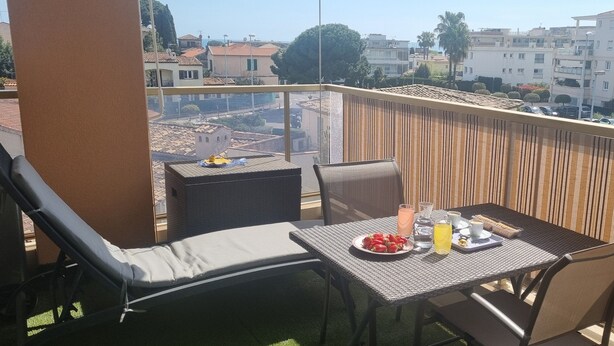 A balcony with a table set for two, a chair, and a sun lounger.