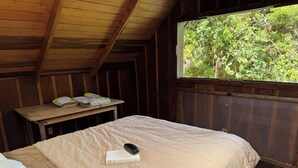 Una habitación de madera con una cama, una ventana y una mesa con objetos encima.