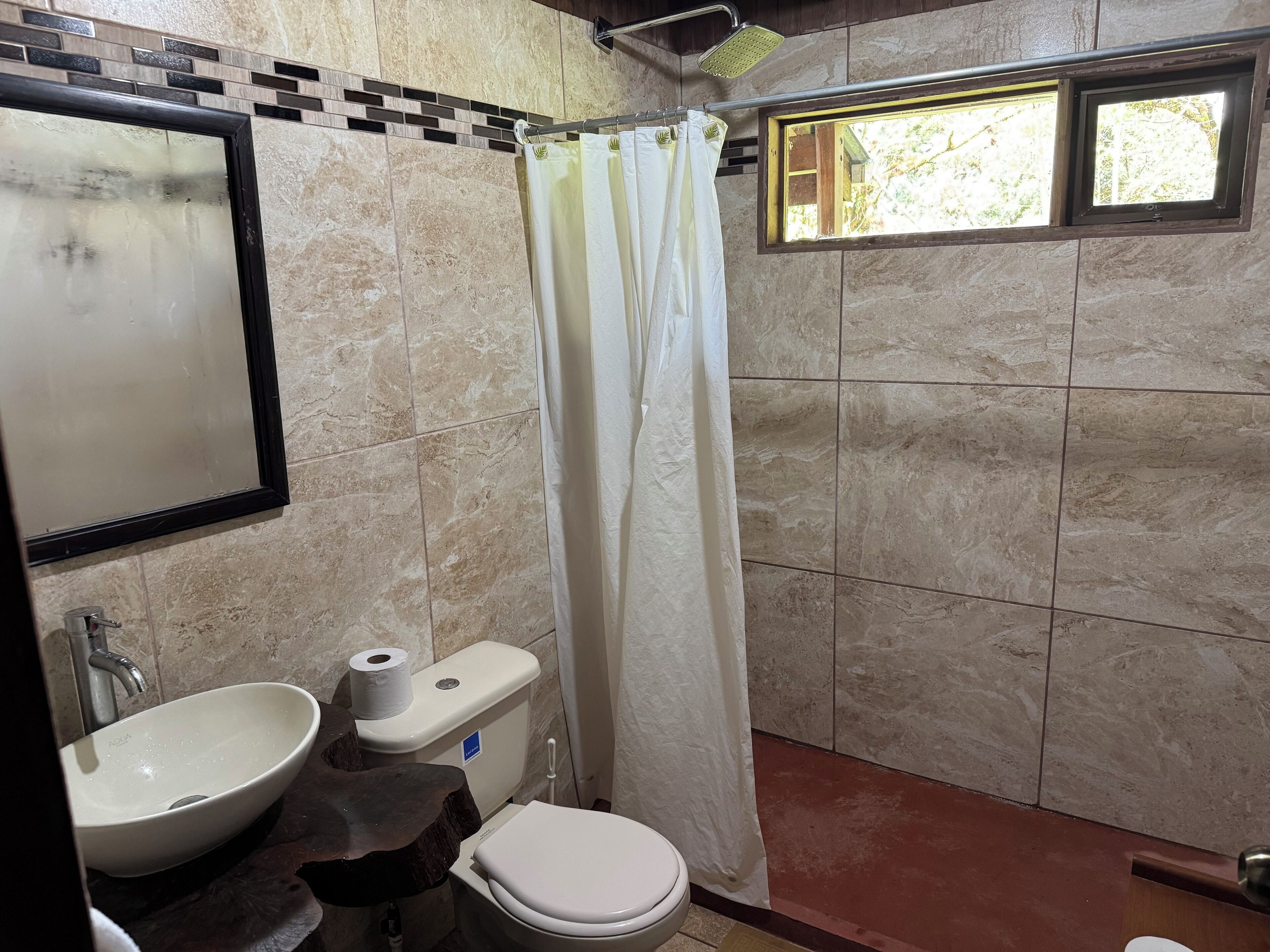 A bathroom with a sink, toilet, shower, and a window.