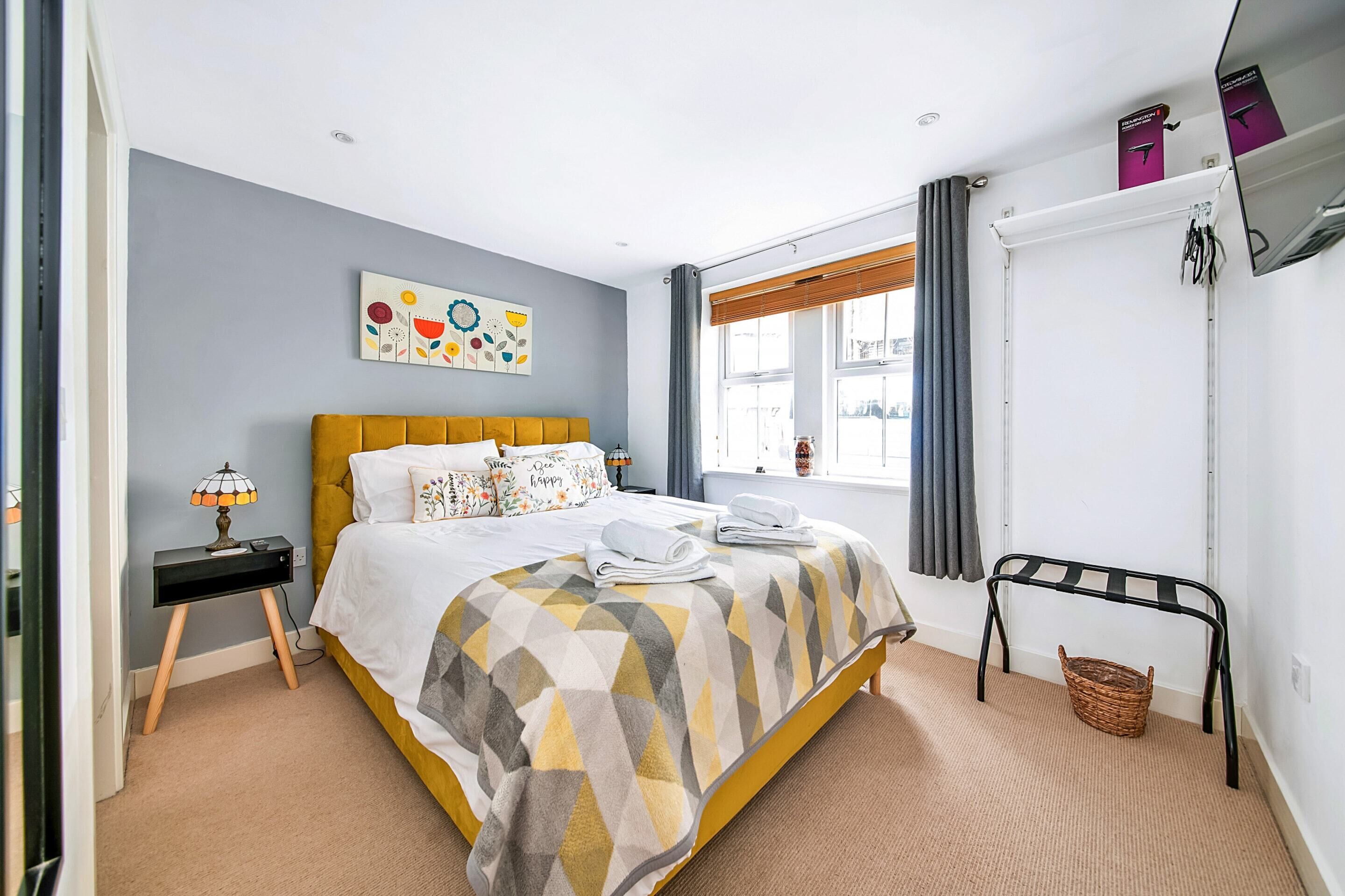A bedroom with a bed, a nightstand, a lamp, a window with curtains, a wall art piece, and a radiator.